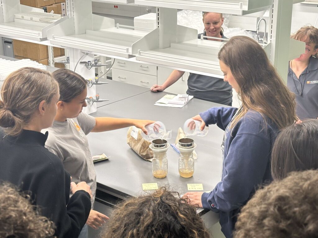 This photo features Dr. Wooliver demonstrating high school students the concept of water infiltration and erosion.
