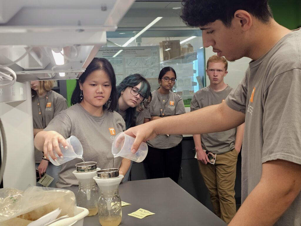 This photo features high school students pouring water to simulate the water infiltration and erosion in tilled and no-till soils.