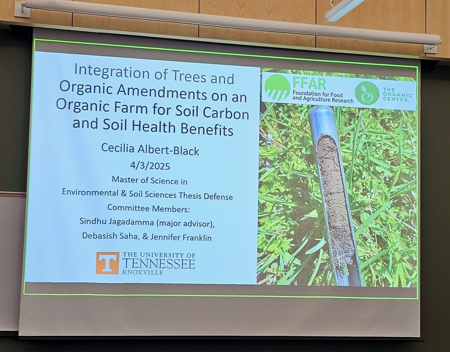 The photo presents the title of Cecilia's defense presentation on the projector as "Integration of trees and organic amendments on an organic farm for soil carbon and soil health benefits."