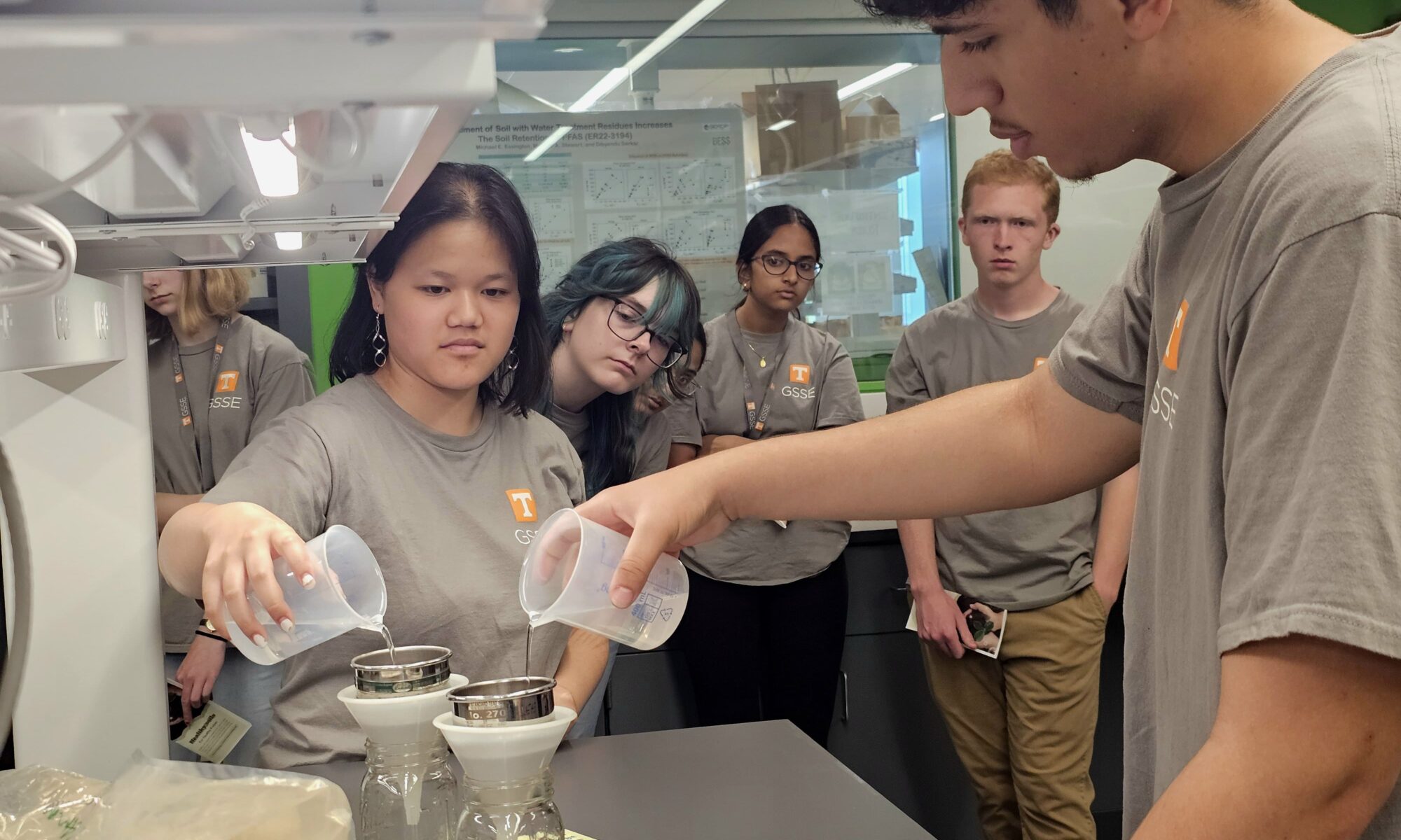 This photo features high school students pouring water to simulate the water infiltration and erosion in tilled and no-till soils.